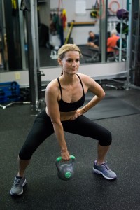 Squat with a wide stance holding kettle bell with an overhand grip. As you rise, lift your elbow toward the ceiling.